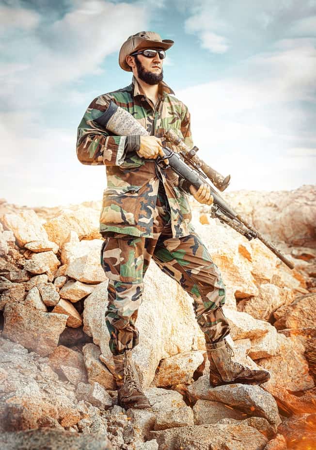 חייל מזוקן עם כובע ומשקפיים מחזיק רובה צלפים